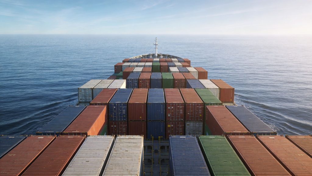 A massive cargo ship loaded with numerous colorful shipping containers sailing on the vast open ocean.